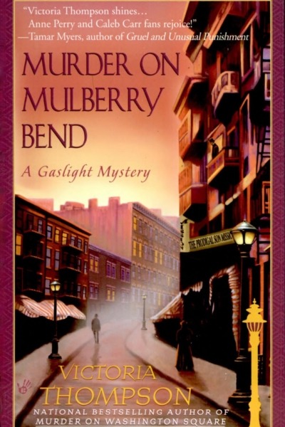 Murder on Mulberry Bend by Victoria Thompson book cover shows a bending, foggy New York City street in the early 1900s. It's dusk and gas street lamps are lit. A man and a woman walk past each other at a distance.