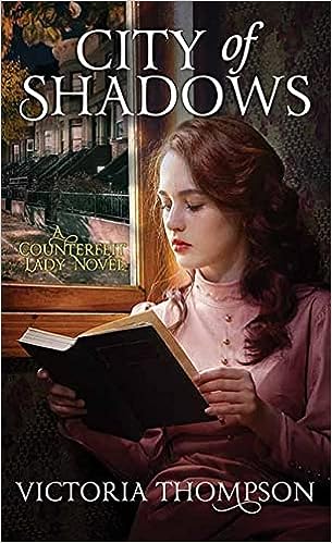 City of Shadows by Victoria Thompson library binding shows a young white woman with auburn hair in a pink early 1900s dress reading by window light.